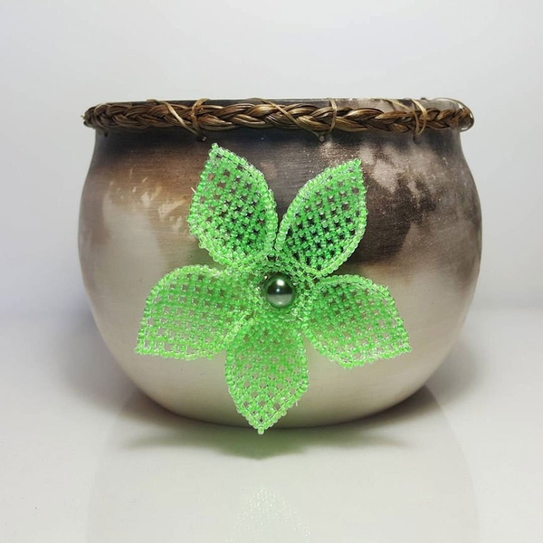 A ceramic pot with braided sweetgrass and a beaded flower.